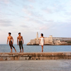 Two topless men and a woman in a white dress beside the sea