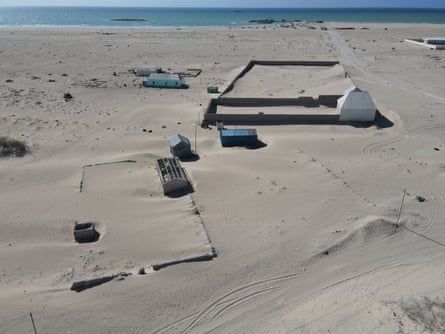 Outlines of walls surrounding homes can be seen almost buried by sand|445x333.75