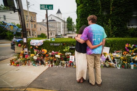Two people hold each other at a memorial on a street corner