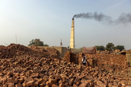 Huge piles of bricks with a smoking chimney in the background. On one pile are bamboo poles and mosquito nets.