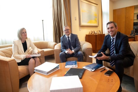 Anthony Albanese, Katy Gallagher and Jim Chalmers are sitting in arm chairs around a round low coffee table. There are books and stacks of papers on the table