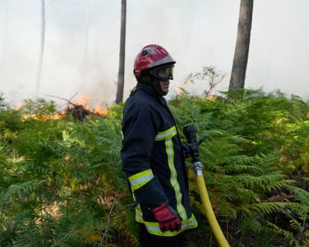 A firefighter holding a hose near flames.