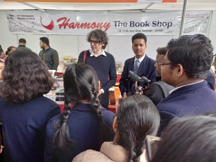 A man with curly hair stands in front of a crowd of school children.