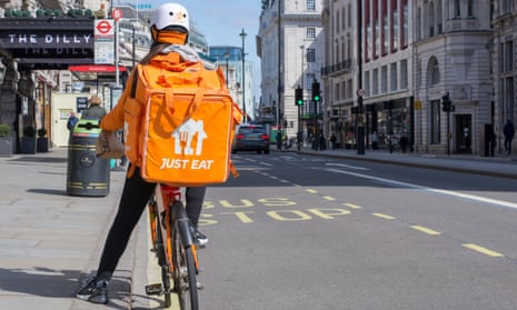 A person stopped by the side of the road on a bike carrying an orange-coloured Just Eat food delivery bag