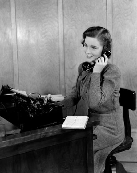 A black and white shot of a smiling receptionist who is taking a phonecall on a landline phone in the 1940s.