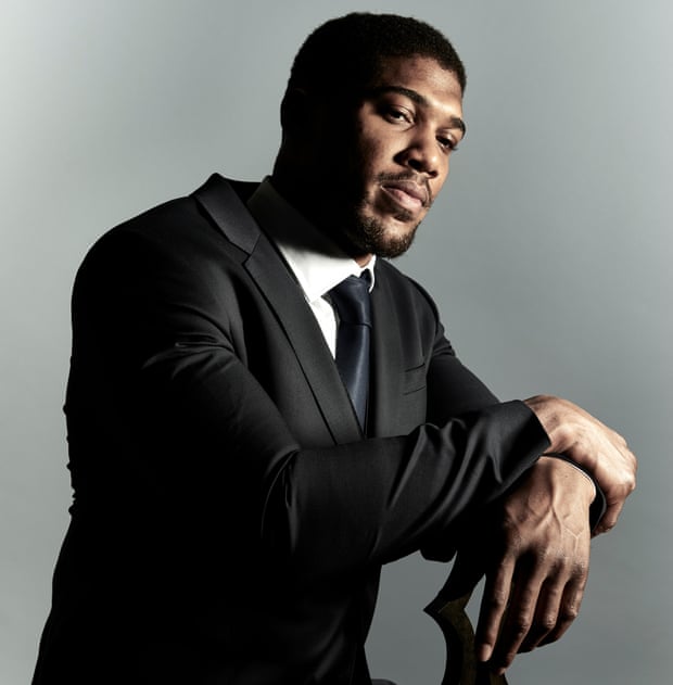 Anthony Joshua sitting on a seat wearing a black suit