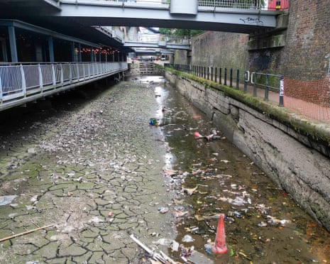 Dried, cracked bed of Manchester's Rochdale Canal strewn with rubbish beneath a footbridge
