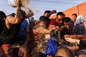 Rum splashes into the air as a man pours it from a bucket held over his head, while others reach forward to place their hands on the statue