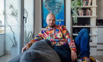 Artist sitting on sofa in living room wearing colourful psychedelic jumper