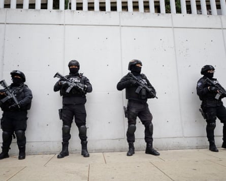 Four heavily armed Investigative police officers guard line up against a wall.