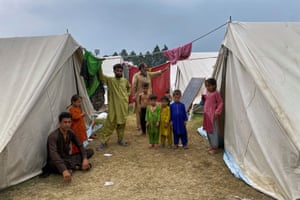 A family of adults and young children in bright clothes stand next to two large white canvass tents
