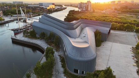 Modern, beautifully designed building on banks of a city river at sunset or dawn.