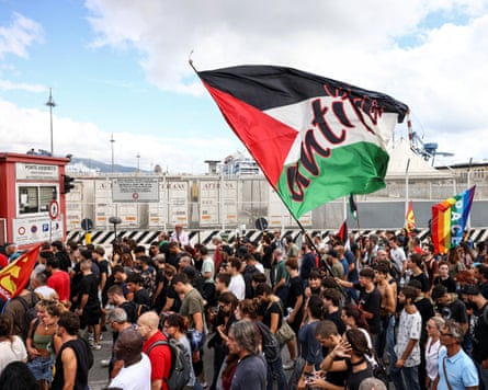 Una multitud de manifestantes, uno de ellos ondeando una gran bandera palestina, afuera de las puertas del puerto.