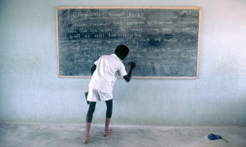 A schoolboy writing on a chalk blackboard in a classroom in Nigeria