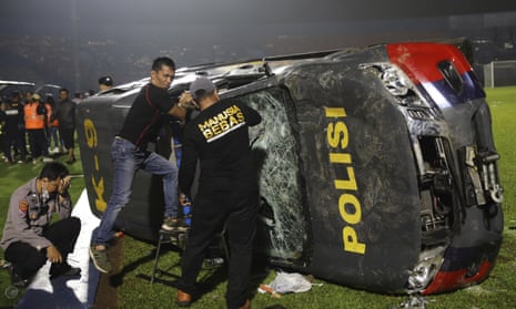 Indonesian officers with an overturned police car on the pitch of the Kanjuruhan stadium in Malang after the clashes