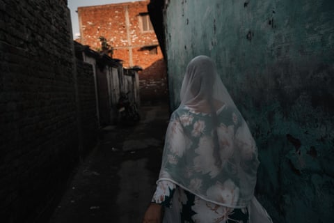 A woman in a white veil wand flowery dress is walking through a dark alley