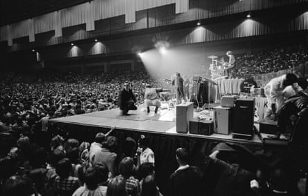 The band performing on a stage in a massive venue surrounded by a large crowd