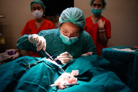 Dr Bow, in surgical clothing, performs an amputation with two veterinary staff in the background