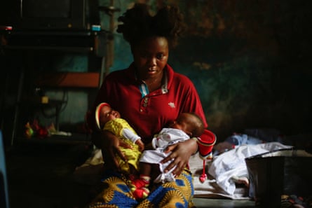A dazed-looking young girl holds two babies in her arms