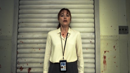 A woman stands with her back to a metal shuttered door that is flecked with blood stains