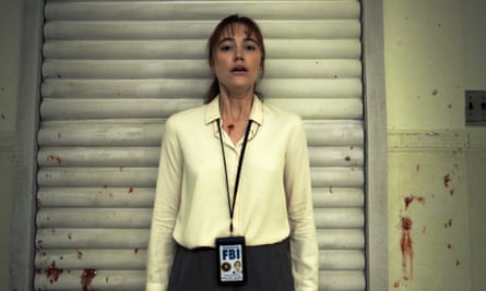 film still of a woman in a yellow blouse and FBI badge looking scared with blood spatters behind her