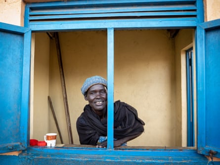 A smiling woman looks out of a blue-framed window with shutters