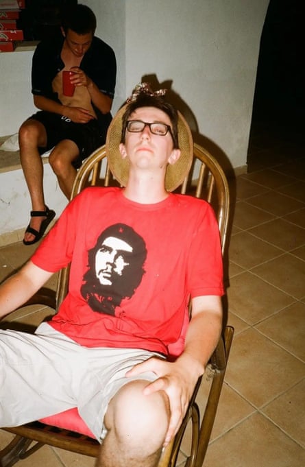 Stewart wearing glasses, a red T-shirt with a picture of Che Guevara on the front and light-coloured shorts, leans back in a chair with his eyes half-closed