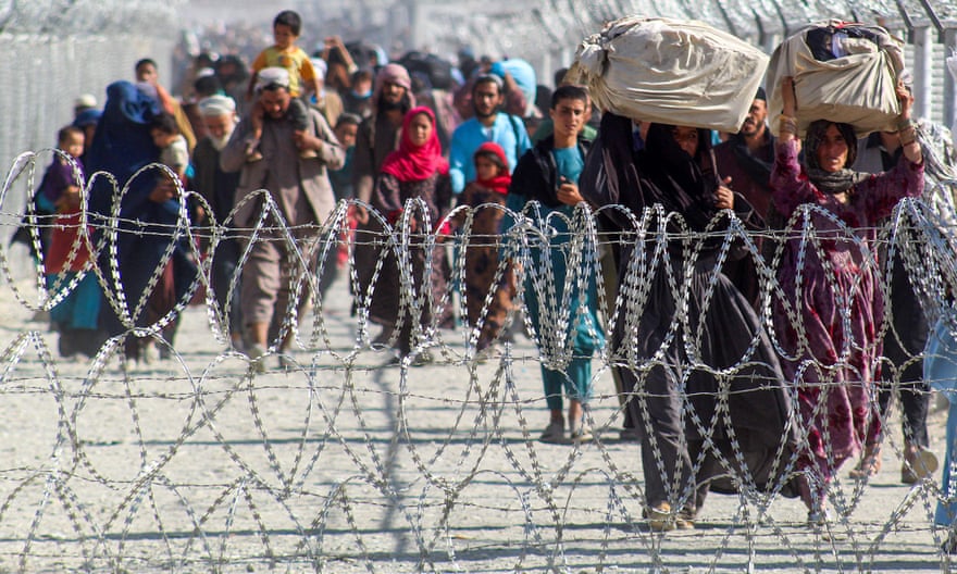 Afghans walk beside barbed-wire fences as they arrive in Pakistan through the border crossing point in Chaman
