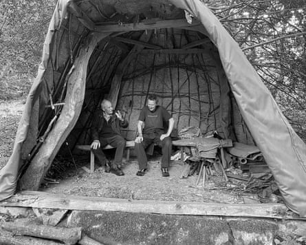 David Nash and Mike Perry sit talking on a bench inside a wooden shelter covered with tarpaulin