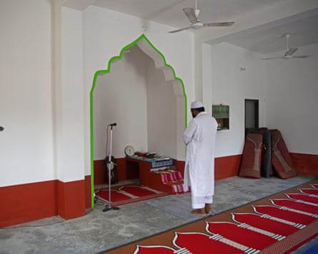 A man in white robes and cap prays facing an arched niche in a rebuilt mosque
