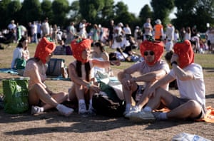 Spectators wearing strawberry hats sit in a park in Wimbledon