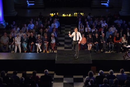 Iestyn Davies wearing a white shirt and black tie on a raised platform surrounded by a seated audience