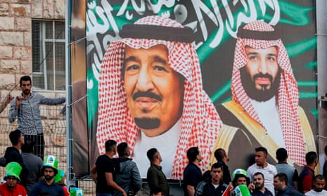 Saudi football fans stand beneath a banner depicting King Salman bin Abdulaziz and his son Crown Prince Mohammed bin Salman.