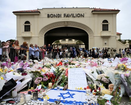 People stand near flowers laid as a tribute at Bondi beach to honour the victims of the terror attack
