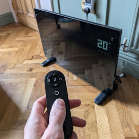 A Devola wifi-enabled smart glass panel electric heater on a wooden floor, with the writer pointing the remote control at it