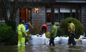Council workers and sandbags next to a flooded house.