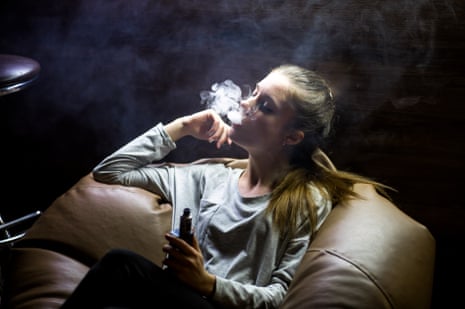 A white teenage girl sitting on a huge brown leather cushion vaping