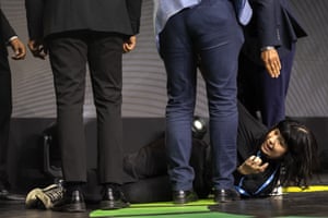 A woman lying on the floor surrounded by the feet and legs of four men