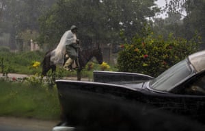 A man, using a piece of plastic as protection against the rain caused by Hurricane Ida, rides his horse on a road leading to Batabano.