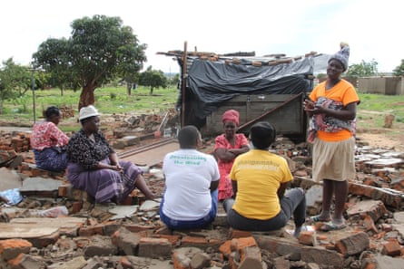 A despondent-looking African family sit amid the rubble of their home