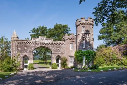 A gothic revival gatehouse with trees around it and a road through it at the Monzie estate in Perthshire