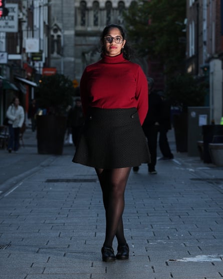 Jaishree Malik stands on a Dublin street at dusk in a red turtleneck and black skirt