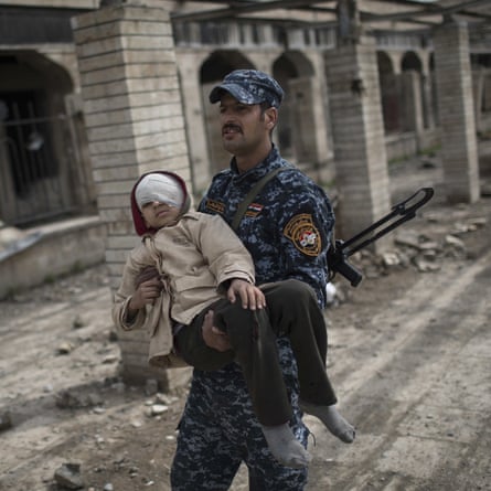 A federal police officer carries an injured boy through a destroyed train station during fighting