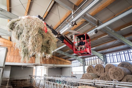 A man operating machinery to move bales of straw in a large modern barn