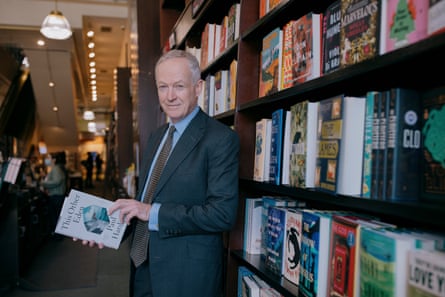 He stands in a Barnes & Noble store in New York next to a display shelf holding a copy of This Other Eden by Paul Harding. He has short grey hair and wears a dark grey suit