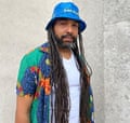 A man with dreads wears an Ikea bucket hat and colourful shirt and white vest.