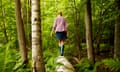 A woman in wellingtons walking along a fallen tree trunk,in woodland.