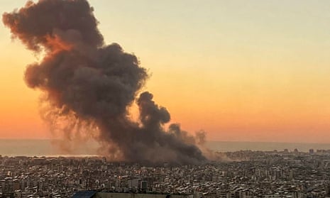 Smoke rises up from a city skyline at sunset
