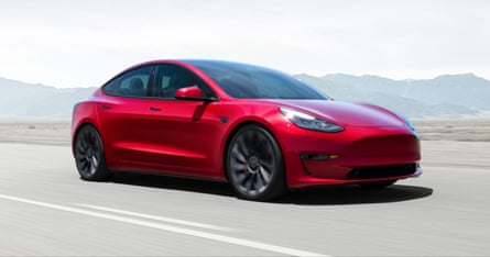A dark red Model 3 Tesla drives a long a vast straight and empty road