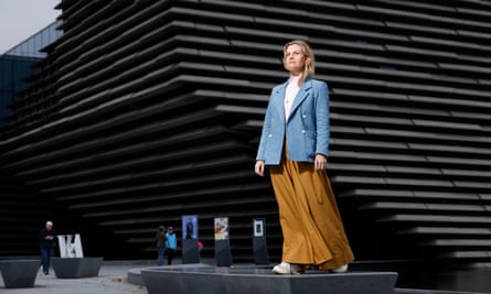Leonie Bell stands, striking the attitude of a sculpture, outside an angular modern building